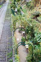 Metal arches supporting shrubs over a path running alongside railway tracks. Parc de Ruisseau, Paris
