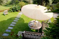 Wooden table, parasol and benches in lawn in Italian garden. 