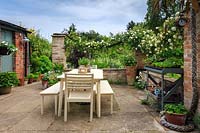 The sheltered patio featuring cream-painted table and chairs, and Rosa 'Alberic Barbier' trained along swags of thick rope