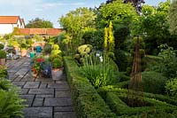 View across garden with stone flagged patio to the left and box topiary -  Buxus sempervirens garden to the right