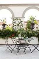 Dining area on classic roof terraces with large planters and urns in archways with view to town beyond