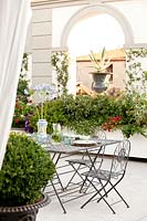 Dining area on classic roof terrace with large planters and urns in arched window with view to town