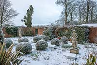 View across sunken walled garden, with balls of Phillyrea angustifolia dusted in snow and statue of Artemis -Diana looking on. 