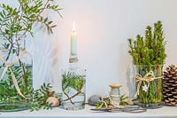 Wooden shelf decorated with a candle in a bottle and freshly cut green foliage