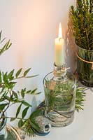 Wooden shelf deocrated with a candle in a bottle and freshly-cut green foliage