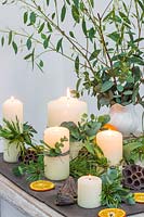 Winter themed table decoration using candles, oranges, seed heads and freshly cut foliage