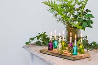Colourful miniature glass bottles used as candle holders decorated with Fern, Ivy and moss