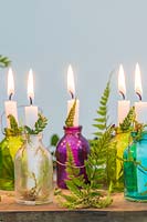 Colourful miniature glass bottles used as candle holders decorated with fern fronds