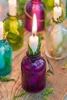 Colourful miniature glass bottles used as candle holders decorated with fern fronds