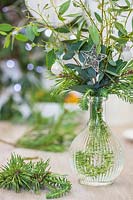 Table decoration featuring a glass vase filled with foliage decorated with silver stars and mini baubles