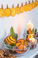 Shelf decorated with clove-studded oranges, candles and Laurus nobilis - Bay, above orange slices pegged up in a line 