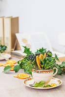 Table decorations including teacup filled with Holly, Ivy berries, Pine foliage and dried orange slices