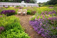 A brick path and seating area with wooden seats in the The Perennial Meadow at Scampston Hall Walled Garden, North Yorkshire, UK. 
