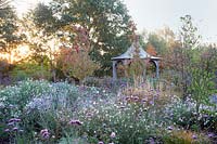 Central pavilion surrounded by autumn planting of grasses, Verbena, Gaura, Asters, Boltonia and Rosa.  Radcot House, Oxfordshire, UK