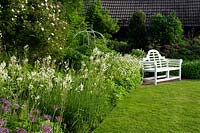 White Lutyens bench in corner of cottage garden. 