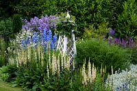 Delphinium 'Summer Skies' in blue and white themed border with obelisk. 