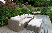 Centranthus ruber behind rattan sofa with footstool and cushions next to hammock on modern decking 