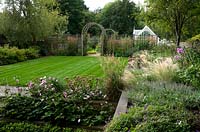 Raised borders and central lawn in modern country garden. 