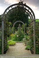 View through trellis arch to obelisk in central raised bed. 