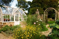 Small greenhouse in vegetable garden with roses in central bed with obelisk. 