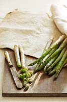 Green asparagus spears, some cut up with knife, on a chopping board