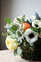 Floral basket display filled with rose 'catalina', dianthus 'antique', eryngium, muscari, pomegranates and white anemones