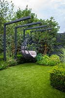 View across small lawn to black swing seat and borders with Gaura lindheimeri 'Sparkle White' and Osmanthus x burkwoodii