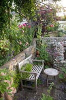 Wooden bench and small table in sunken walled folly surrounded by self-seeding plants