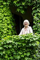 Woman stands on a balcony covered in green foliage