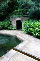 Water feature pond fed by rill, gravel path and stone tunnel arch through earthwork