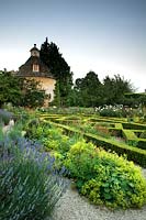 View over Lavendula - Lavender - and Alchemilla mollis in gravel to parterre with pigeon house beyond
