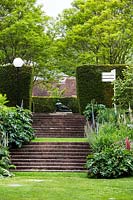 Steps between borders including Dicksonia antartica, echium pininama, rheum palmatum, hosta 'big daddy'. leading to sculpture. Bourne garden. Glyndebourne. Uk