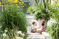 Children play on the terrace with container grown perennial grasses and herbaceous plants