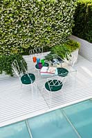 Table and chairs in modern terrace garden surrounded by evergreen planting.