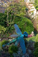 Verdigris dragonfly sculpture in plant bed