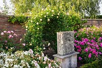 Carving on plinth surrounded by roses in The Victorian Walled Garden
