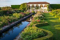 Wide water rill with double borders of roses and serpentine edging on either side, loggia beyond 
