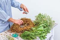 Woman using floristry wire to hold moss onto metal wreath form frame. 