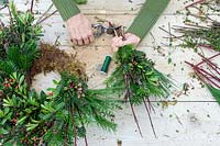 Woman using secateurs to trim stems of a bundle of winter foliage and cuttings
