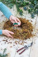 Woman using floristry wire to attach moss to wire wreath form. 