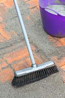 A soft brush being used to push polymer sand into joins of newly laid brick path