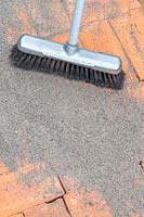 A soft brush being used to push polymer sand into joins of newly laid brick path