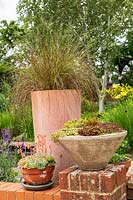 A group of terracotta containers with ornamental grasses and Sempervivum on a low brick patio wall