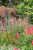 A border with mixed perennial planting including Penstemon and Linaria purpurea, and rusted metal poppy seedhead supports