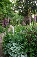 Sundial in a perennial border by a gravel path, plants include: Digitalis - Foxglove, variegated Brunnera and Astrantia 