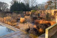 Contemporary design within an old walled garden, view across beds of ornamental grasses and shrubs planted in blocks 