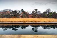 Reflections in long rectangular pool surrounded by grasses and trees.