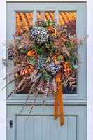 Rustic orange, green and blue Festive wreath hung on stable style front door