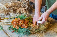 Man using floristry wire to attach moss to wreath form