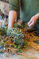 Man using floristry wire to attach dried hydrangea heads onto wreath